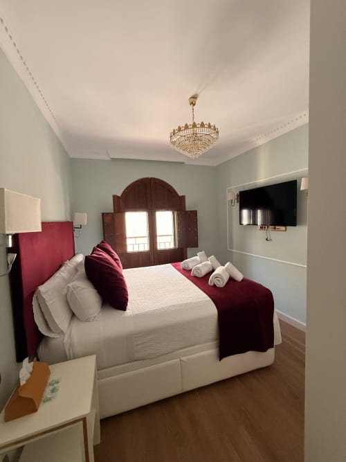 Dormitorio elegante en Edificio San Esteban 16, Sevilla con ropa de cama blanca, acentos burdeos y araña ornamentada
