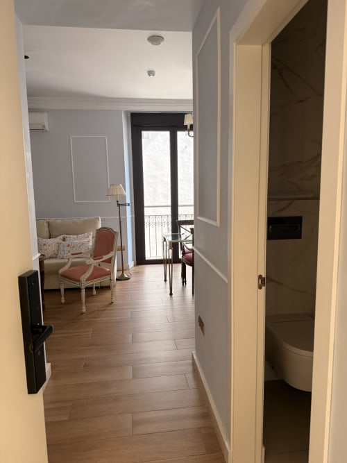 Pasillo de suite moderna en Edificio San Esteban, Sevilla con suelos de madera, paredes color crema y vista al salón con balcón