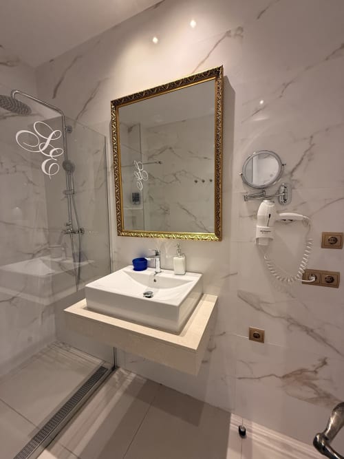 Baño moderno de mármol en suite de hotel sevillano con espejo enmarcado en dorado, lavabo tipo recipiente y ducha de efecto lluvia