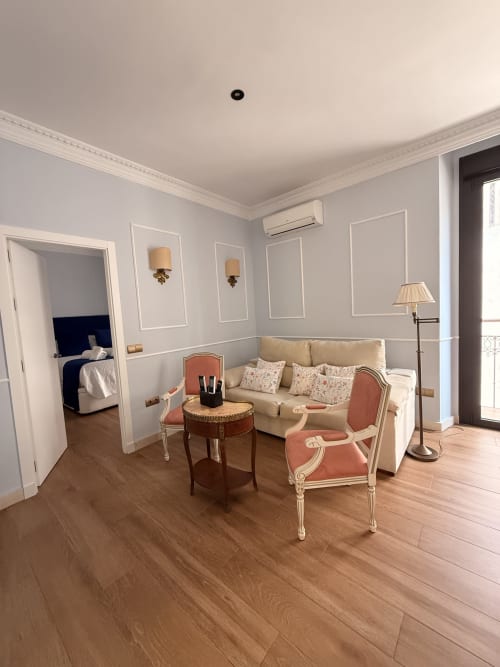 Elegante sala de estar de la suite Sevilla con sofá crema, sillón coral, suelo de madera y acceso al balcón