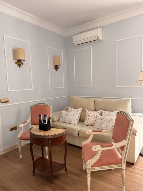 Suite elegante en Edificio San Esteban 16, Sevilla con sofá crema, sillas coral, mesita de madera y pared decorativa