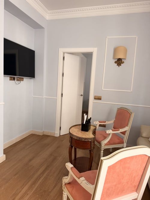 Elegante suite de dormitorio en Edificio San Esteban 16 Sevilla con sillas coral, mesa de mármol y TV de pantalla plana