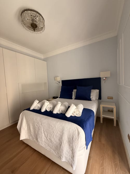 Suite moderna en Edificio San Esteban 16 en Sevilla con cabecero azul marino, ropa blanca, toallas enrolladas y detalles de madera