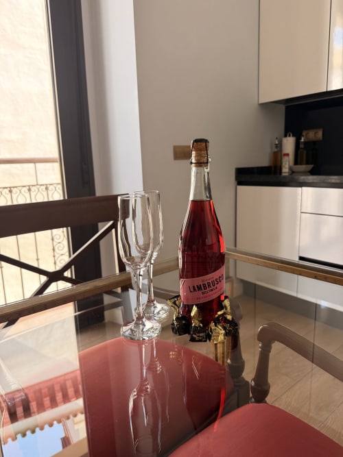 Botella de Lambrusco con copas de champagne en mesa de comedor de suite de hotel en Sevilla con vista a la cocina