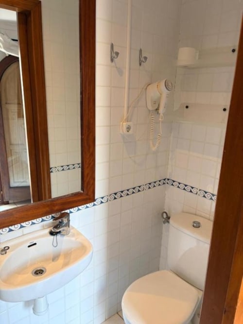 Baño con azulejos blancos, cenefa decorativa azul, lavabo, inodoro y ducha en habitación Hotel Oliva, España