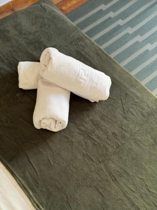 Toallas blancas enrolladas dispuestas sobre una cama verde en la Hotelito Oliva Pensión, Oliva
