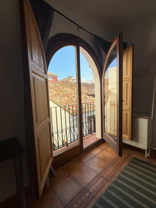 Puerta arqueada que abre a un balcón con vistas a los tejados de terracota de Oliva, España en Hotelito Oliva Pensión