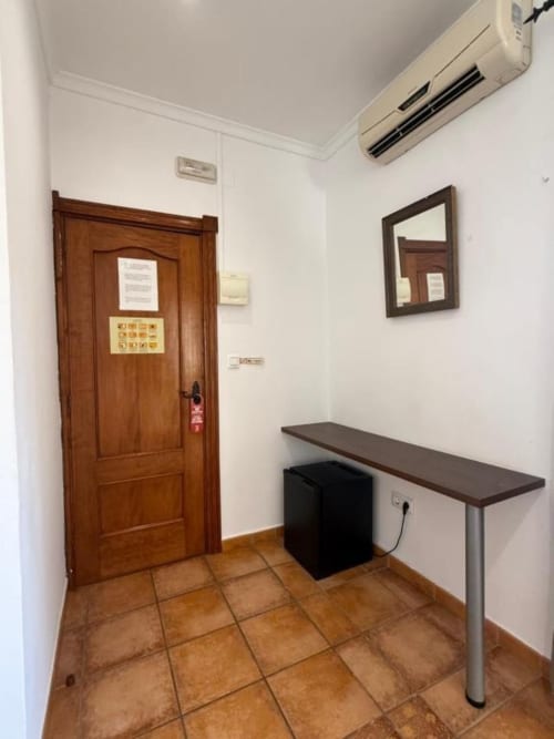 Pasillo de entrada del Hotelito Oliva Pensión en Oliva con puerta de madera, consola, espejo y aire acondicionado