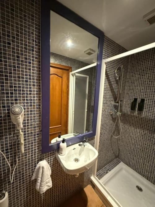Baño moderno en Hotelito Oliva Pensión de Oliva con lavamanos pequeño, cabina de ducha, paredes con azulejos oscuros y espejo enmarcado