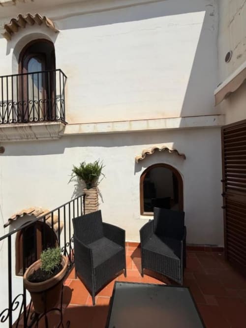 Soleado patio del Hotelito Oliva con paredes blancas, puertas arqueadas, plantas decorativas, sillas negras y suelo de terracota