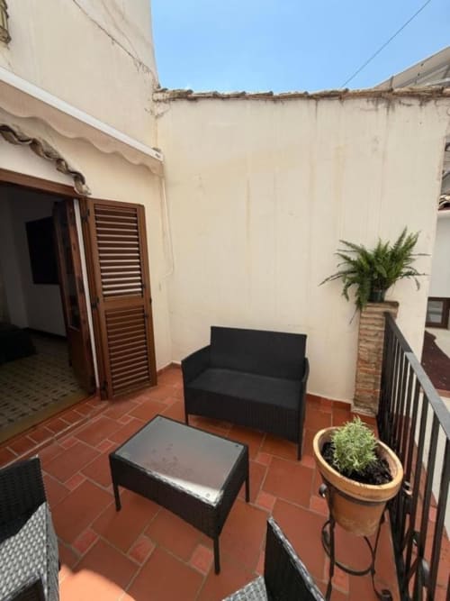 Terraza privada del Hotelito Oliva Pensión en Oliva con asientos negros, plantas en macetas y paredes color crema