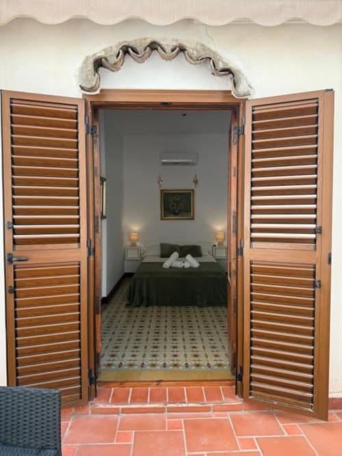 Contraventanas de madera abiertas revelando un dormitorio con ropa de cama verde en Hotelito Oliva Pensión en Oliva, España, con toques de terracota