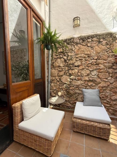 Acogedora terraza con muebles de mimbre y pared de piedra en Hotelito Oliva Pensión, Oliva, España