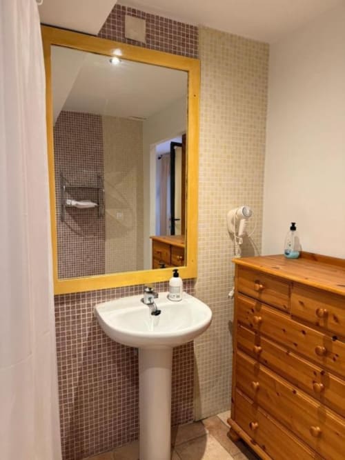 Baño moderno en Hotelito Oliva Pensión con lavamanos pedestal, espejo marco amarillo, azulejos mosaico y cómoda de madera