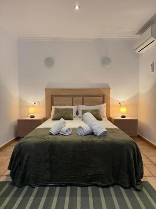 Moderna habitación doble en Hotelito Oliva Pensión con cama de madera, ropa de cama verde, lámparas gemelas y altavoces de techo blancos