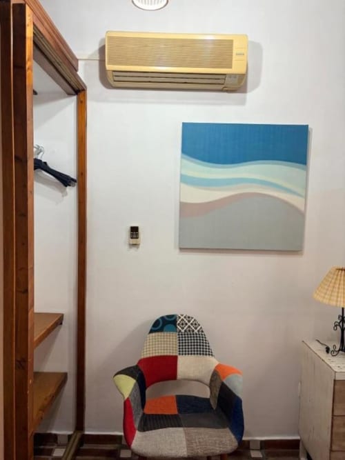 Habitación moderna en Hotelito Oliva con silla patchwork colorida, unidad de aire acondicionado beige, obra costera abstracta y