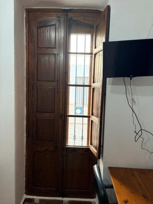 Puertas de madera oscura abriéndose a un balcón con vistas al mar en Hotelito Oliva Pensión en Oliva, España. Habitación moderna con televisor visible.