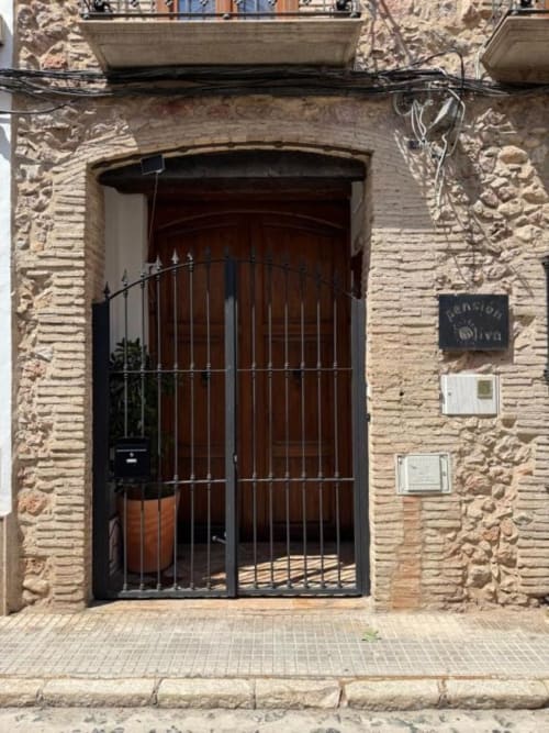 Entrada de la Pensión Hotelito Oliva con fachada de ladrillo tradicional, puerta de hierro forjado y balcón en Oliva, España