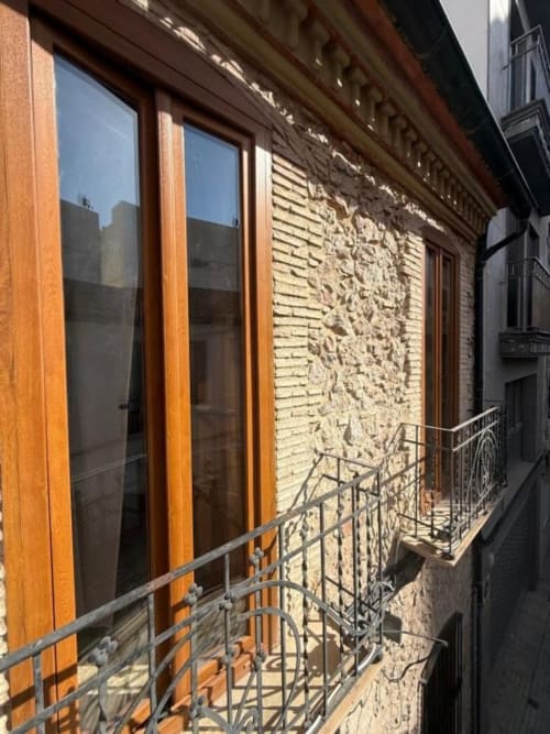 Balcón con barandilla metálica con vista a un callejón en Hotelito Oliva Pensión en Oliva, España, con puertas de madera y pared de ladrillo