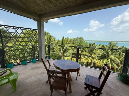Terraza elevada del hostal Cayuco Maya en Bacalar con vista al lago tropical, palmeras, muebles de madera y