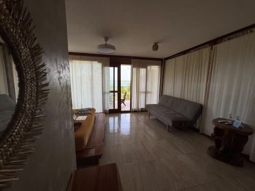 Habitación moderna del hostal Cayuco Maya en Bacalar con sofá gris, pisos de madera y puertas de vidrio hacia la terraza con vista al lago