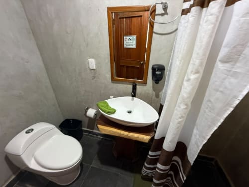 Baño moderno del hostal Cayuco Maya en Bacalar con inodoro blanco, lavamanos ovalado y cortina de ducha