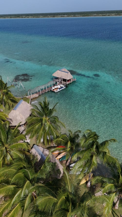 Vista de la laguna turquesa del hostal Cayuco Maya en Bacalar con muelle, palapa y palmeras