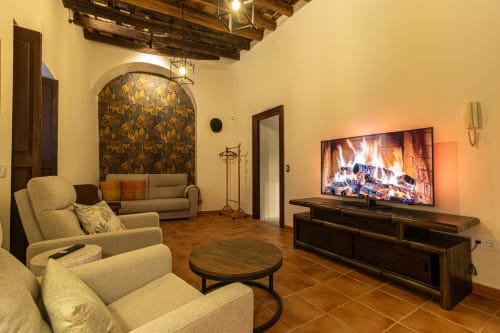 Elegante sala de estar en apartamento Casa Haurie de Jerez de la Frontera con chimenea, TV, muebles beige y vigas de madera