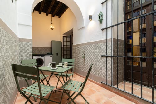 Patio del apartamento Casa Haurie con mesa de comedor, sillas verdes y azulejos andaluces tradicionales en Jerez de la