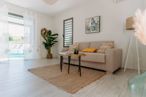 Lumineux salon moderne à l'Habitation l'SEO avec canapé beige, table en bois, plantes et vue sur piscine à Sainte-Anne