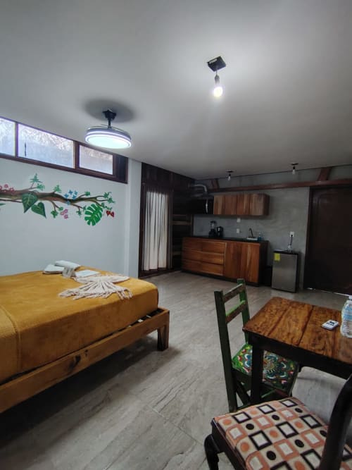 Habitación Tucán del hostal Cayuco Maya en Bacalar con cama, mesa de comedor, cocina y ventiladores de techo