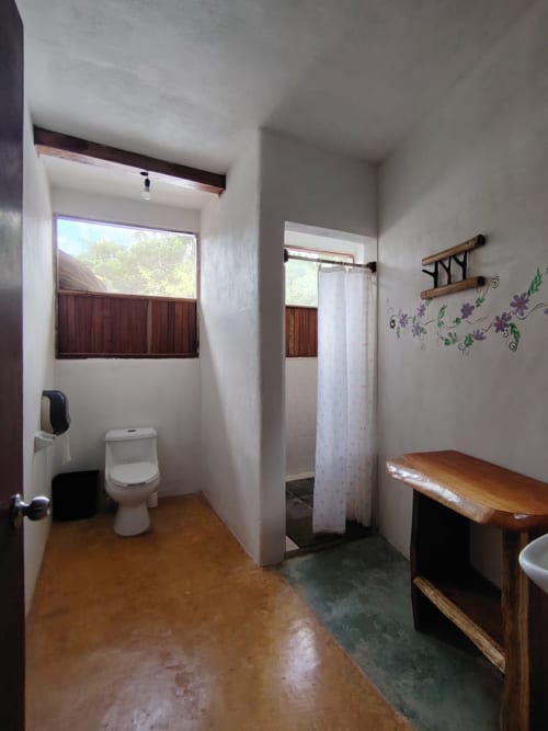 Baño espacioso en habitación Tucán del hostal Cayuco Maya, Bacalar con inodoro, ducha, tocador de madera y ventanas