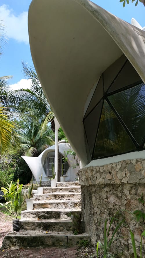 Estructura de glamping con domo geodésico en el hostel Cayuco Maya de Bacalar, con arquitectura curva blanca, escaleras de piedra y ambiente tropical