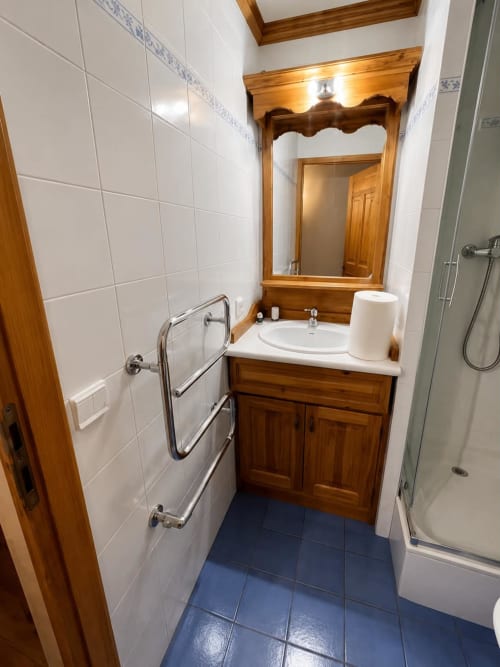 Salle de bains moderne avec vanité en bois, carrelage blanc, sol bleu, miroir et lavabo au Chalet des Cimes, Belle Plagne