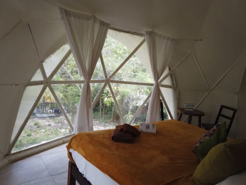Habitación en domo geodésico del hostal Cayuco Maya en Bacalar con vistas al jardín a través de ventanas geométricas y mobiliario