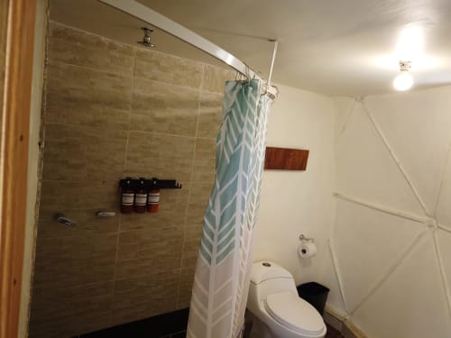 Baño moderno en domo de glamping Cayuco Maya en Bacalar con ducha, inodoro y cortina de baño geométrica