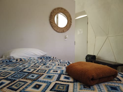 Dormitorio acogedor en el albergue domo geodésico Cayuco Maya en Bacalar con cama, espejo tejido y manta marrón