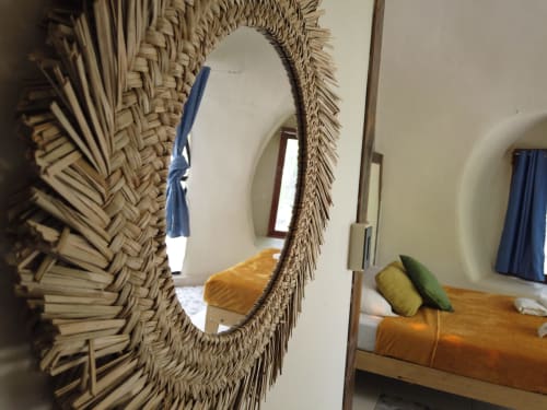 Espejo circular tejido en dormitorio glamping Cayuco Maya con ropa de cama naranja y almohadas verdes en Bacalar, México