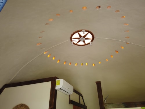 Techo de cúpula geodésica con tragaluz de rueda de madera y luces decorativas cálidas en el hostal Cayuco Maya de Bacalar, México