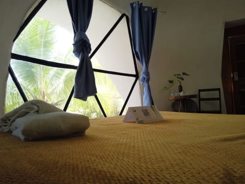 Dormitorio en domo glamping de Cayuco Maya, Bacalar con vista al jardín, toalla enrollada y palmeras visibles por ventana geométrica