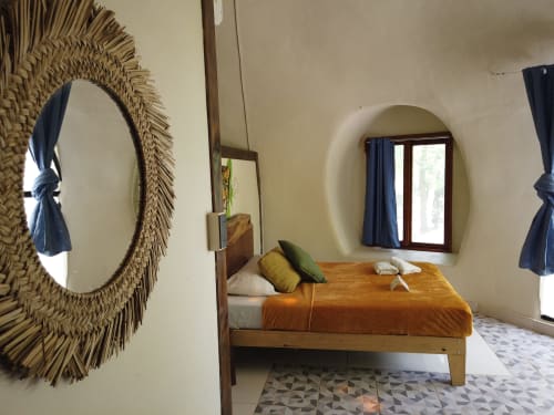 Habitación con domo geodésico en el hostel Cayuco Maya de Bacalar, con cama de madera, espejo tejido y ventana arqueada con vista al jardín