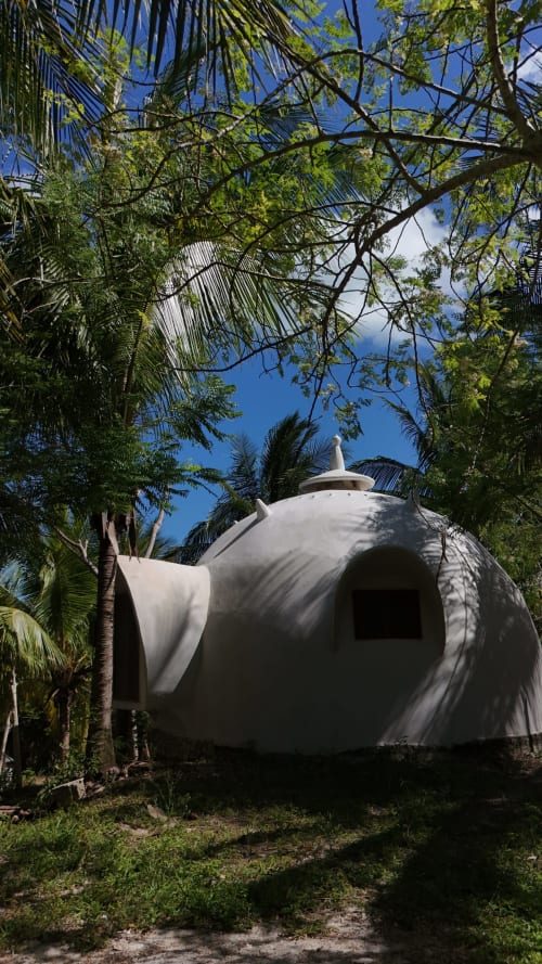 Habitación glamping con domos geodésicos blancos rodeada de exuberante jardín tropical con palmeras en Cayuco Maya, Bacalar, México