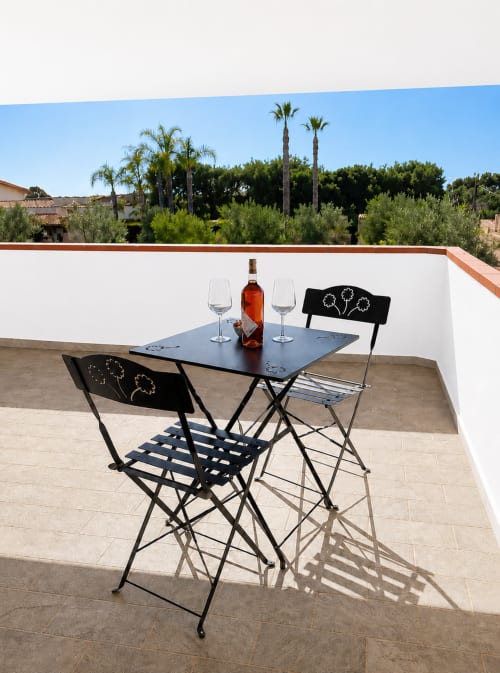 Terrasse extérieure du B&B Helios à Nardò avec bouteille de vin, verres et chaises noires donnant sur un jardin méditerranéen
