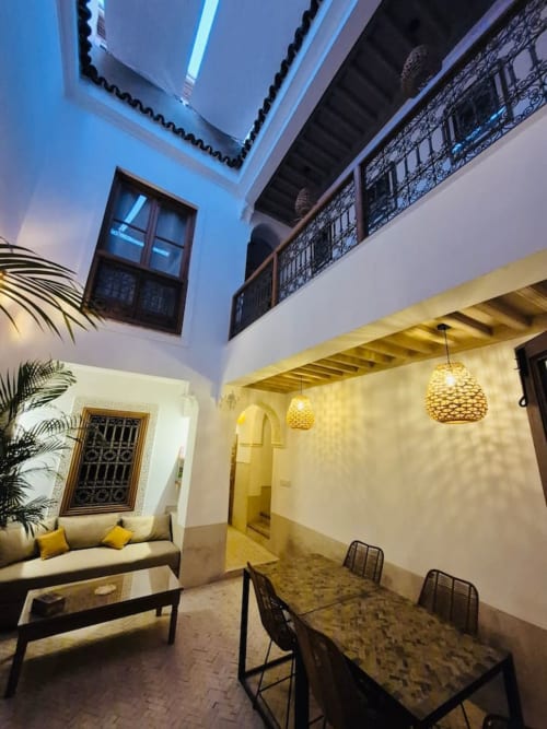 Patio traditionnel marocain avec ciel ouvert bleu, luminaires suspendus jaunes, table à manger et ferronnerie ornementale