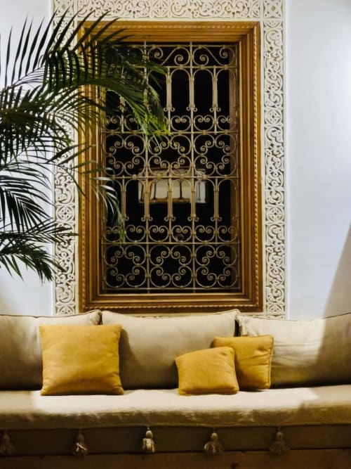 Salon du Riad Casa Angelo à Marrakech avec fenêtre en laiton ouvragé, sièges crème et coussins jaunes