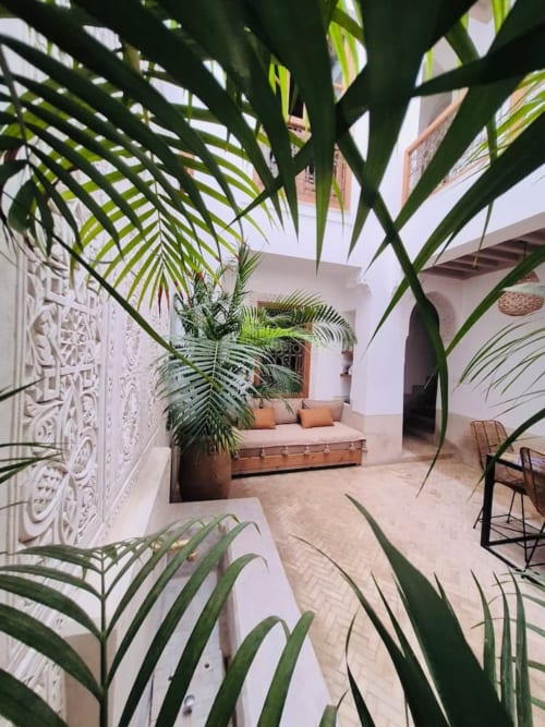 Cour du Riad Casa Angelo à Marrakech avec palmiers, murs blancs sculptés et coin détente