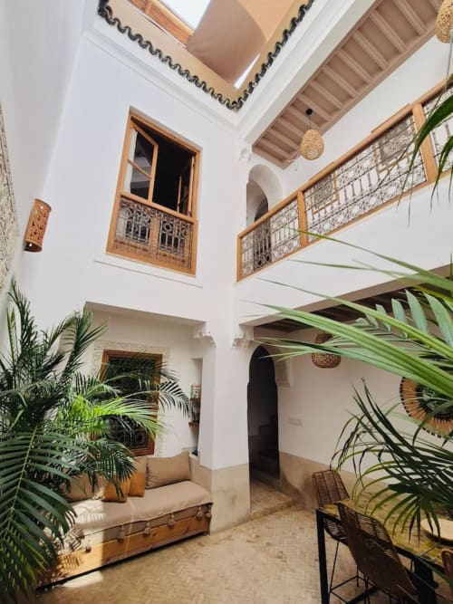 Cour du Riad Casa Angelo à Marrakech avec murs blancs, balcons en bois, puits de lumière et plantes vertes luxuriantes