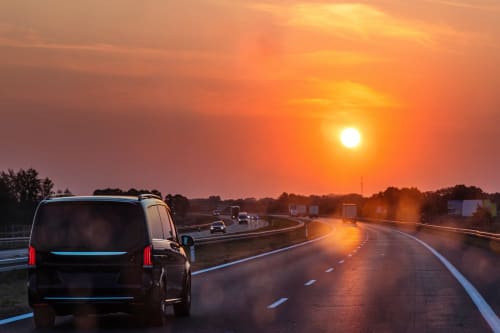 Trafic routier au coucher de soleil avec des véhicules se dirigeant vers le soleil doré sur une route dégagée