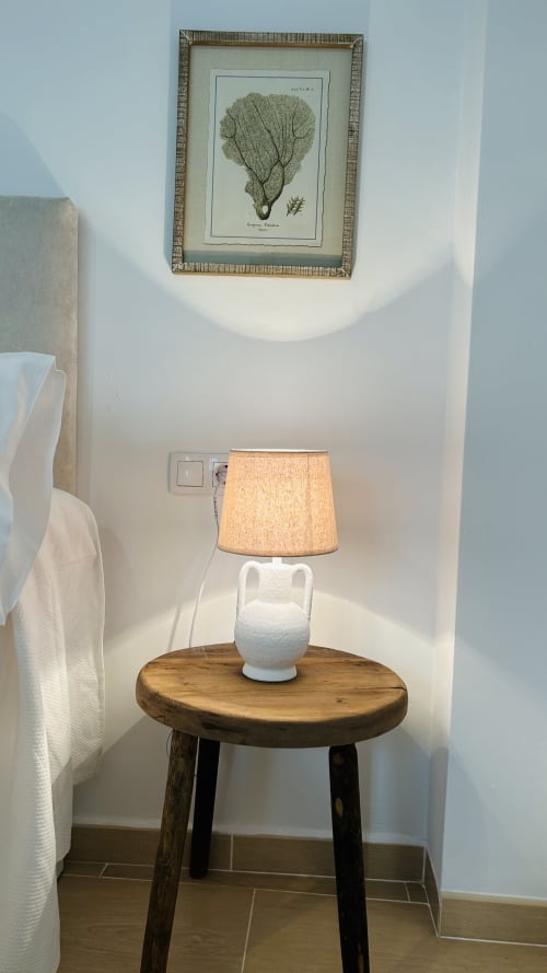 Cozy studio corner at Alojamientos Estrella Baeza with wooden side table, white ceramic lamp, and botanical wall art