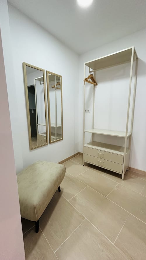 Modern dressing room with mirrored closet doors, white wardrobe storage, and beige ottoman in Baeza apartment